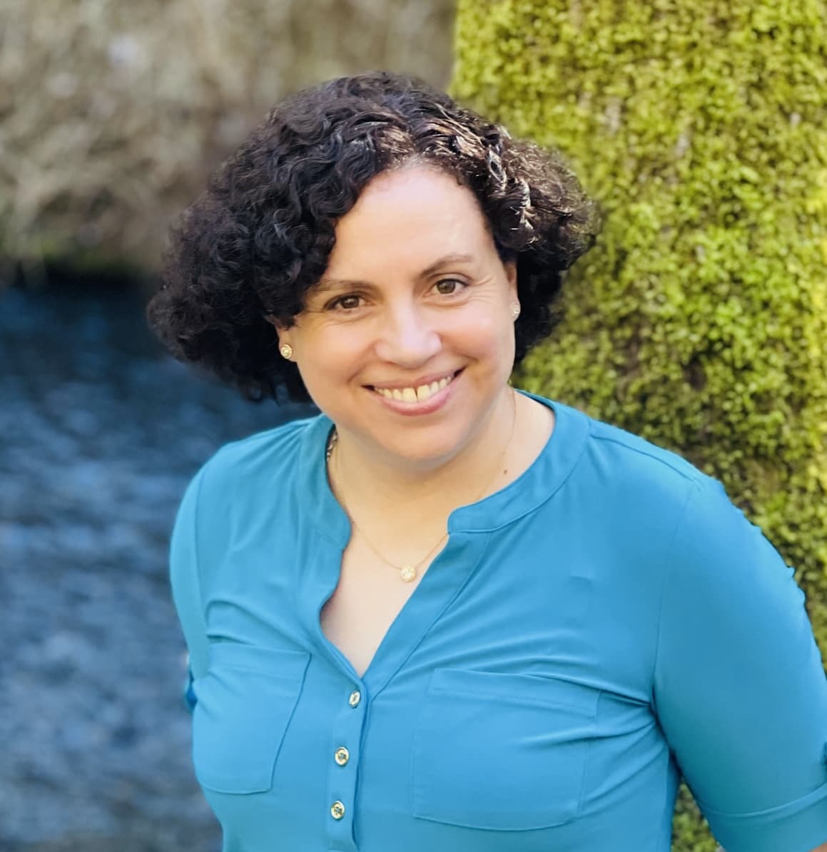 Helena smiling in front of a mossy tree next to a creek